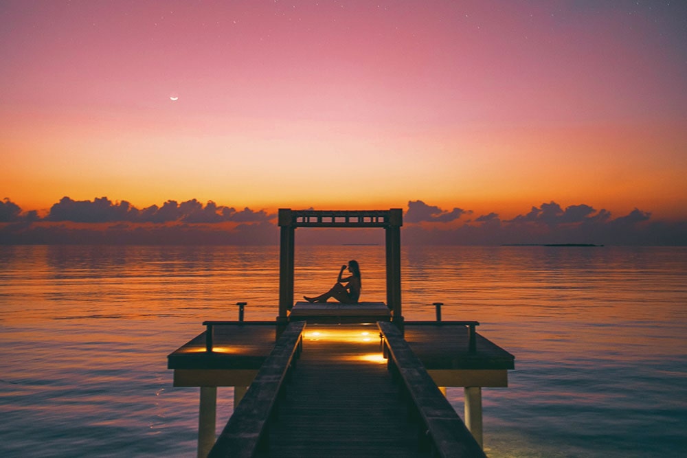 Photo décorative : une femme assise au loin avec un coucher de soleil